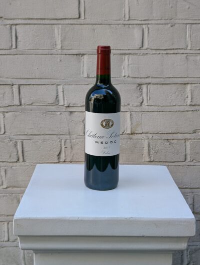 Bottle of Chianti Classico 2022 by Fontodi – organic Sangiovese with cherry, floral, and spice notes from Tuscany- photographed on a white pedestal against a white brick wall.