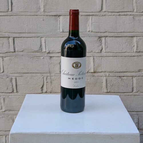 Bottle of Chianti Classico 2022 by Fontodi – organic Sangiovese with cherry, floral, and spice notes from Tuscany- photographed on a white pedestal against a white brick wall.