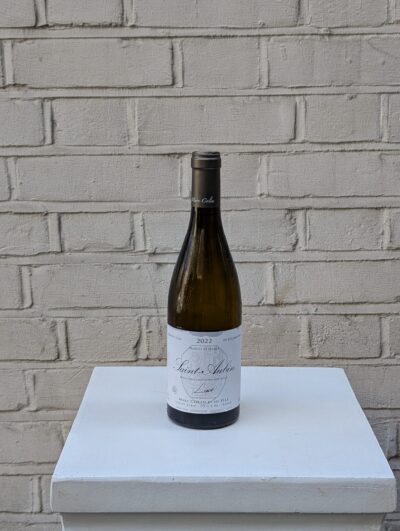 Bottle of Saint-Aubin ‘Cuvée Luce’ 2022 by Marc Colin – Burgundy Chardonnay with citrus, peach, and mineral notes - pictured on a white pedestal against a white brick wall