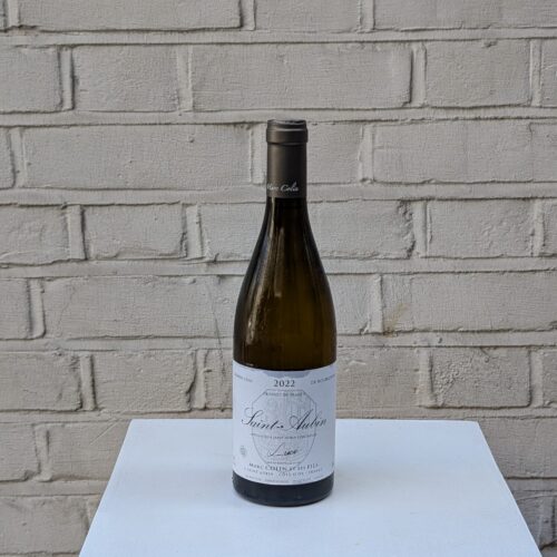 Bottle of Saint-Aubin ‘Cuvée Luce’ 2022 by Marc Colin – Burgundy Chardonnay with citrus, peach, and mineral notes - pictured on a white pedestal against a white brick wall